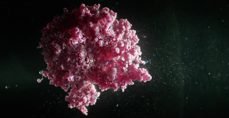 Amorphous blob of pink particles floating on a translucent liquid