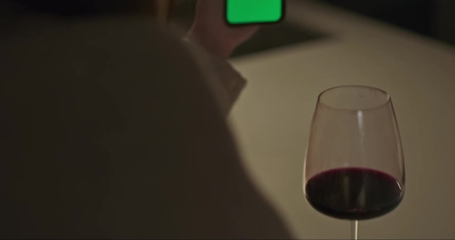Woman looking at the screen of a phone near a glass of wine at home