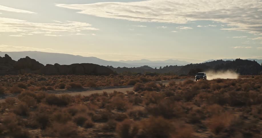 A truck is traveling on a desert road leaving a trail of smoke behind it
