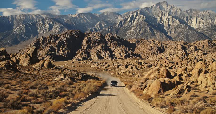 Black suv drives on a dirt road through the desert near the mountains