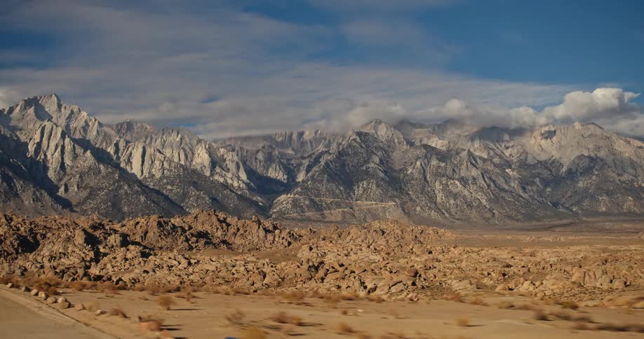 A distant mountan range under the clouds in the desert seen from a moving vehicle