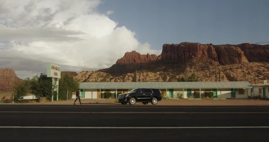 Man walks towards and suv coming out of the parking lot of a motel in the desert