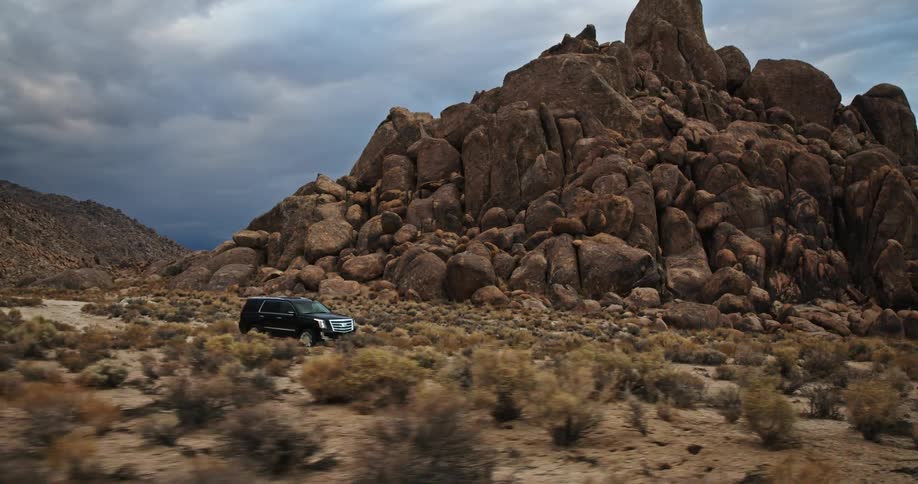 Suv drives along dirt road through arid scrubland near boulder covered hill