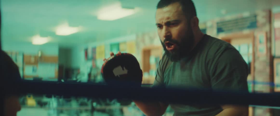 A man wearing pads on his hands encourages his son as he trains him to box in a ring