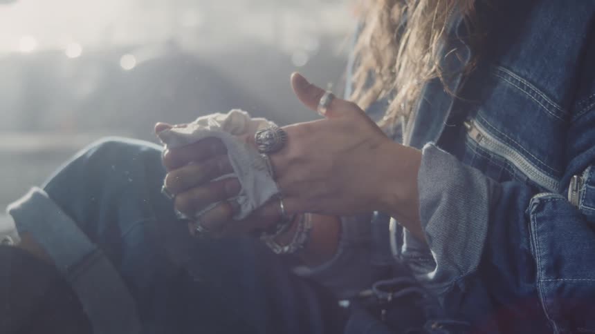 A young female mechanic wearing a denim jacket cleans her hands with a white rag inside a garage