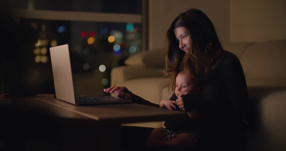 A mother holds her baby as she types on the laptop