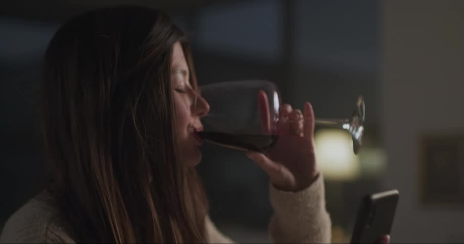 Young woman drinks wine while checking her phone at home
