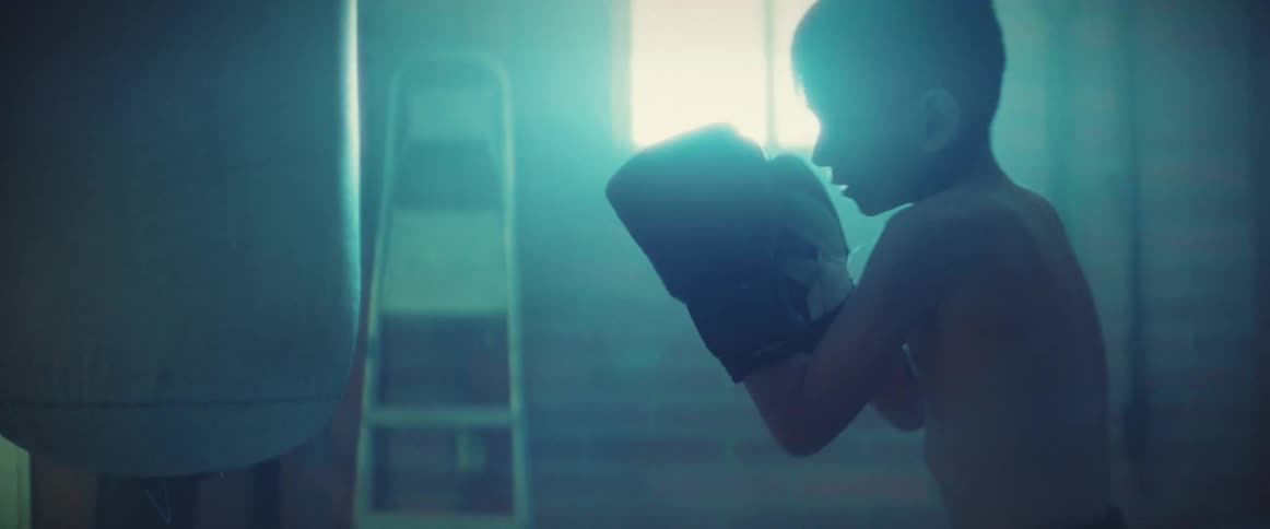 A boy trains by striking a punching bag while the bag is held in place by a trainer