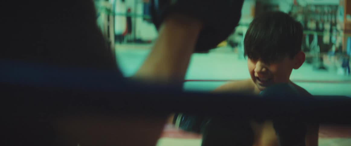 Young boxer trains in ring with adult at a well lit boxing gym