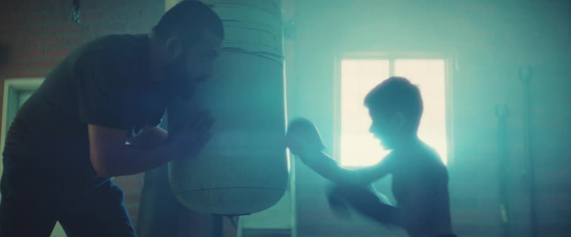 A kid is boxing with a man inside of a gym around the day time