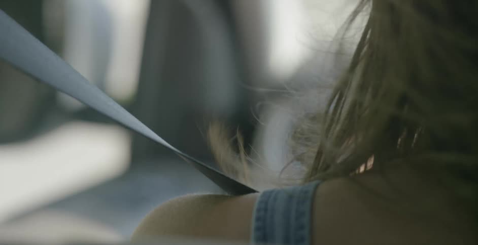 A woman's hair blows in the wind while she drives with the window open in the day time