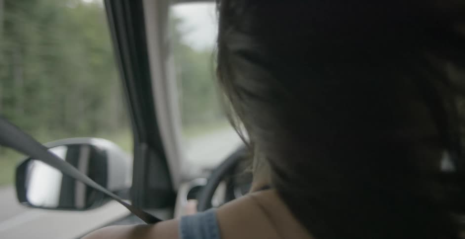 A woman's hair blows in the wind while she drives with the window open in the day time