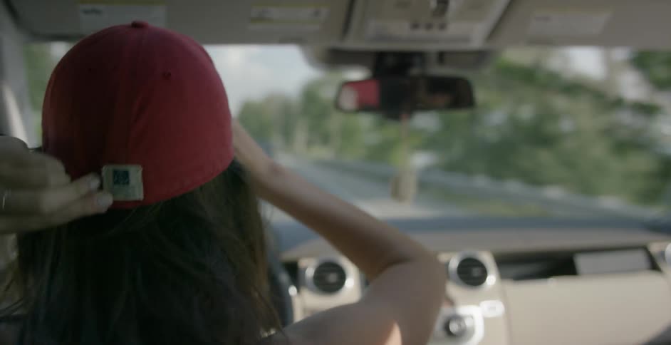 A woman driving a car puts a red cap on her head
