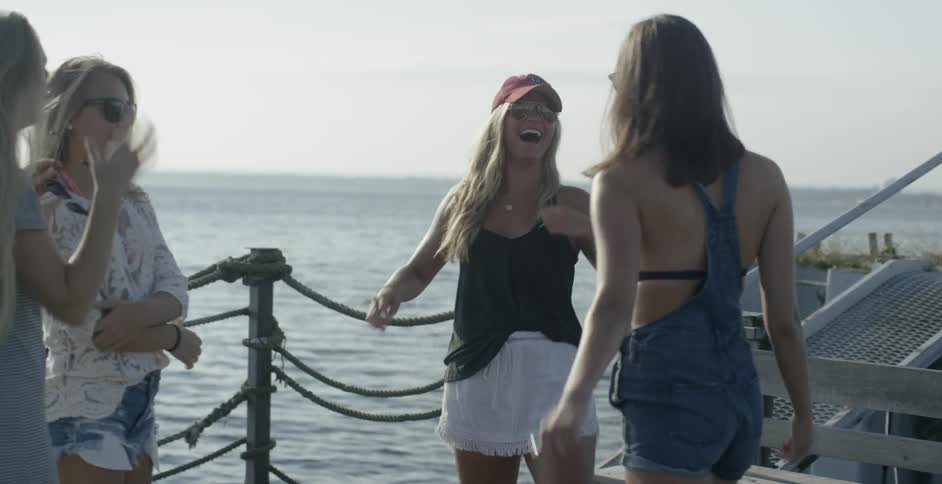 A group of female friends laugh and talk outside near a body of water