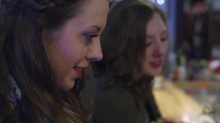 Two women smile and talk at a bar