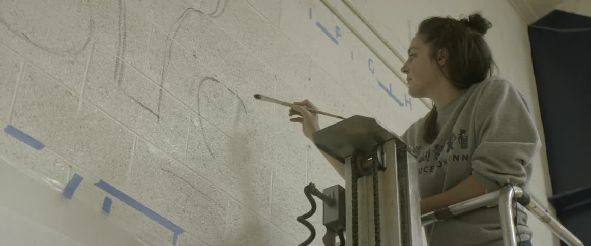 A woman begins a painting on a wall