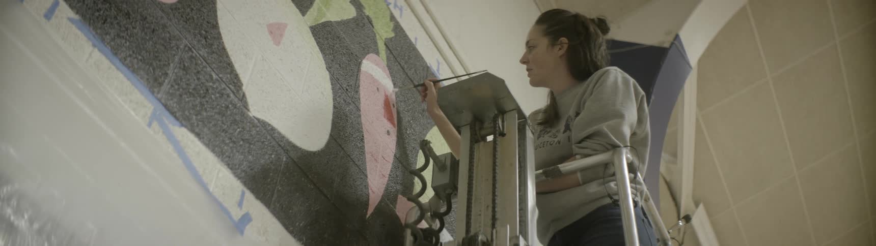 A woman paints a headband on a carrot on a mural