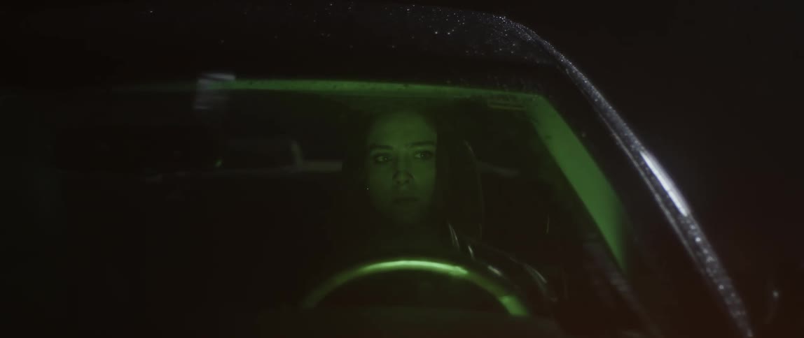 Woman gets into car at night and sits while windshield wipers wipe rain off windshield