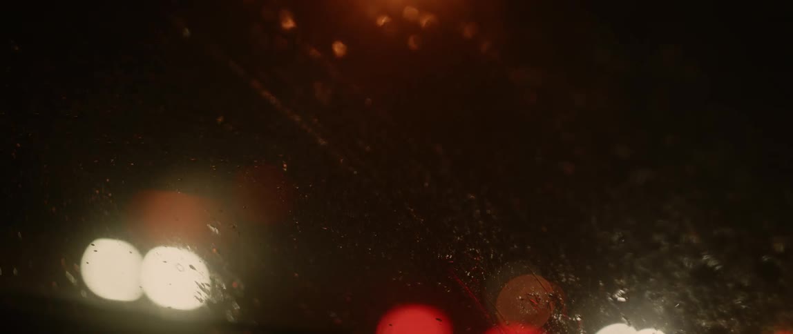 A windshield wiper moves the rain off the window as traffic drives by the car