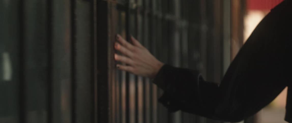 A female runs her hand along bars on a building as she walks down a city street