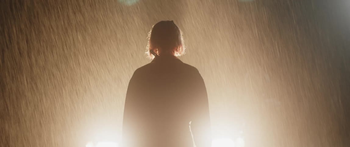 A white man is walking outside in the rain at night time