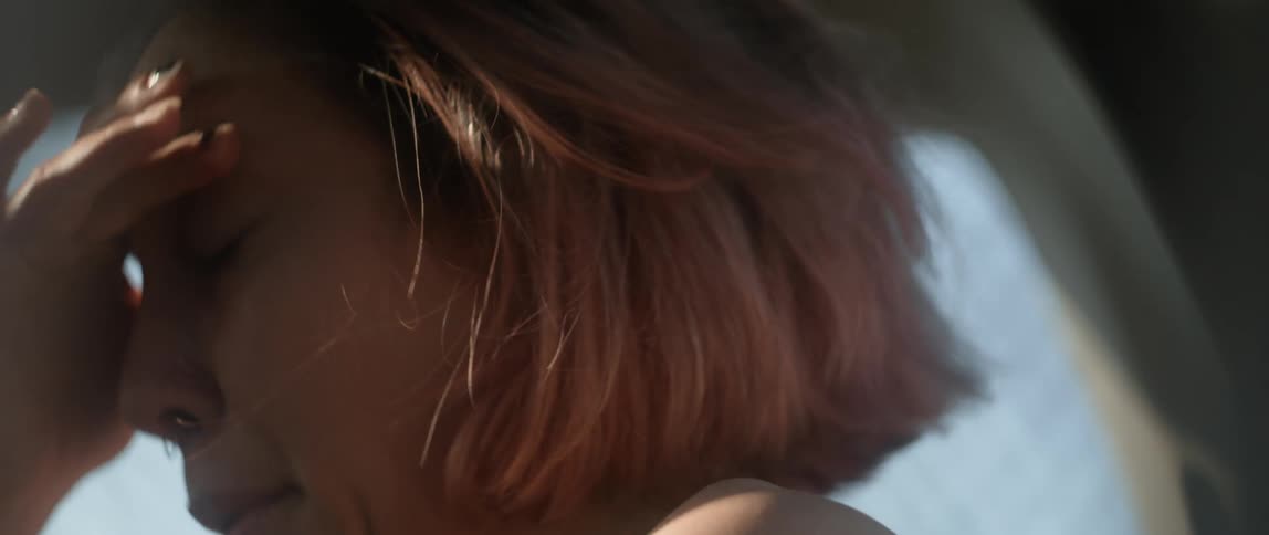 Woman with short hair squints into the sun and rubs her hair and eyes in distress