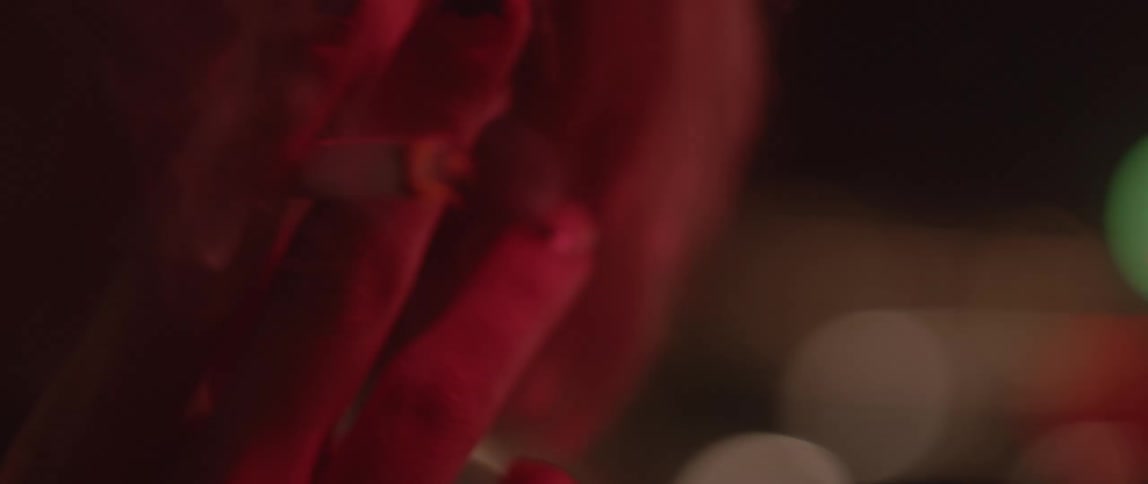 A woman is smoking a cigarette and has lights flashing behind her