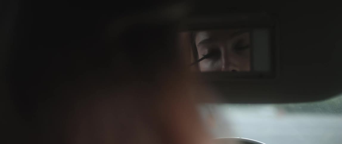 Woman applies makeup using the mirror on a car