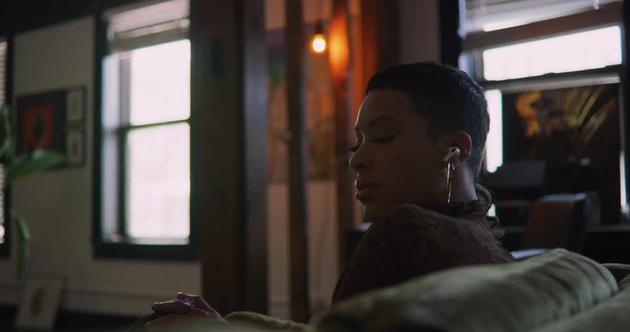 Woman sits on couch wearing earbuds and listening to music