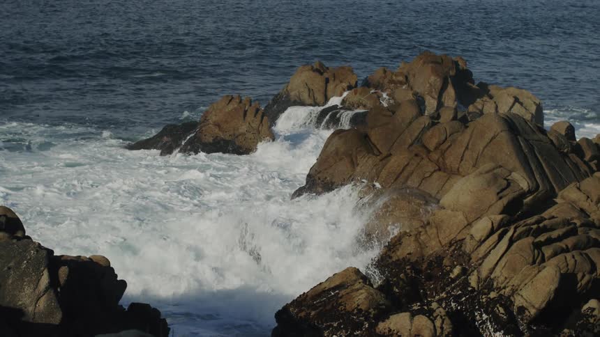 Ocean waves crash upon the jagged rocks that line a coastal area