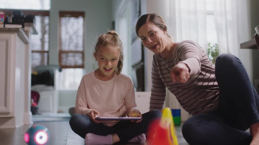 A girl and her mom use a tablet to control a robot toy at home