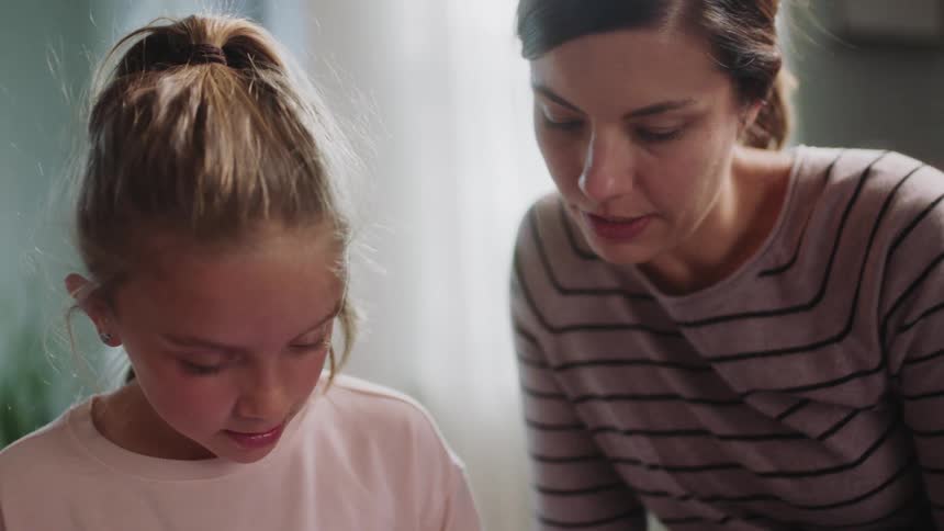 Mother helps girl interact with tablet as they sit on the floor