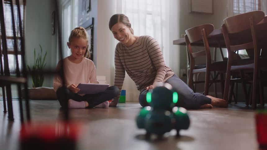A mother and daughter using a laptop to move a robot
