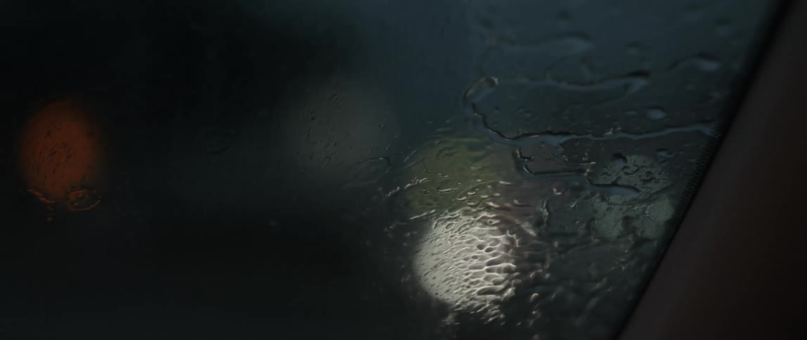Close up of water drops streaking over the windshield on a moving car at night