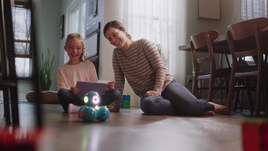 A mother and a daughter on the floor using a laptop to move a robot