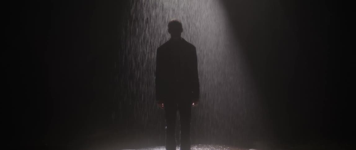 A man is standing outside in the rain at night time