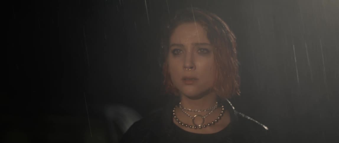 A fearful woman looks into the distance while slowly walking forwards outdoors on a rainy night