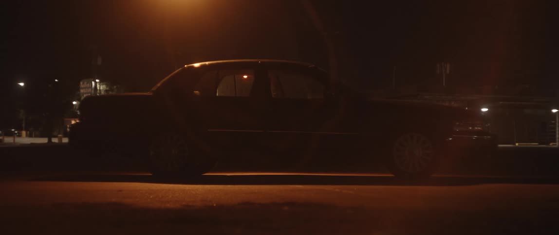 Silhouette of a person sitting on the back of a parked car at night preparing to sleep