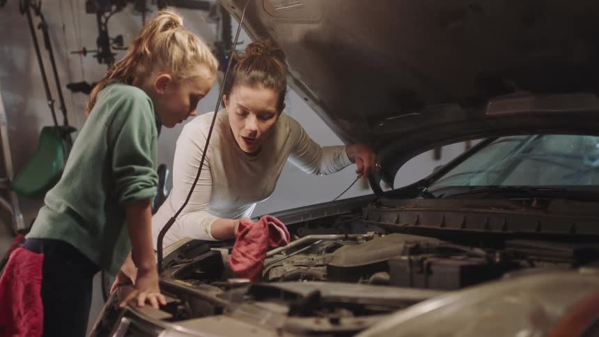 Mother teaching her daughter how to check the oil on a car engine in the garage