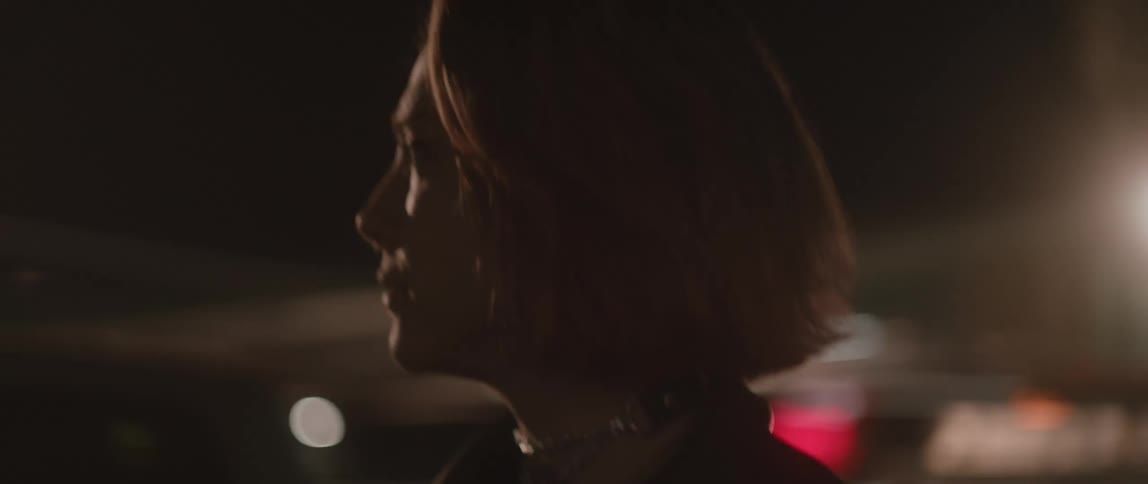 Redheaded woman walks outdoors during night as city lights shine onto her