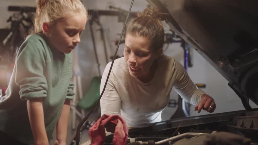 A mother is teaching her daughter how to fix a car