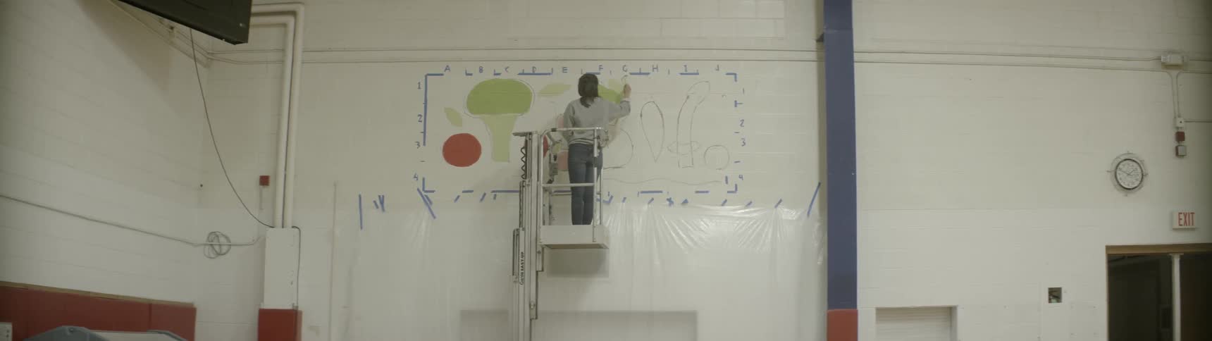 Person on a cherry picker painting a picture high up on the wall