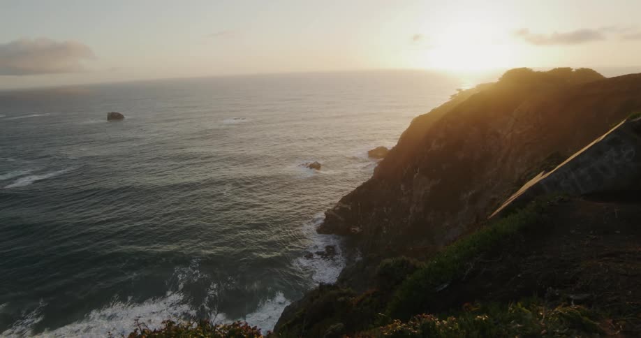Waves roll in against a grassy cliff on a hazy morning