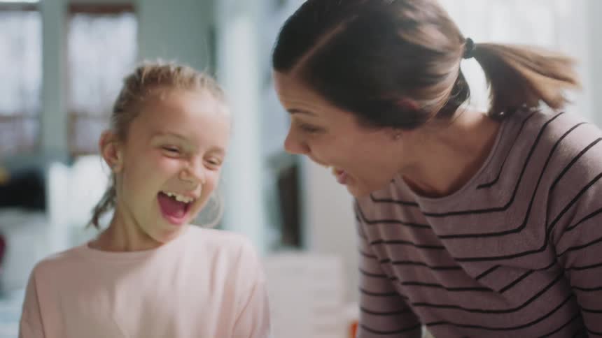 A girl and her mother are sitting in the house laughing as they look at something