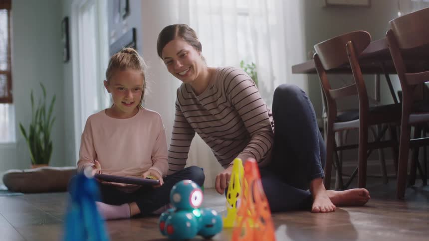 Mother and daughter sitting on the floor on the living room play with a remote control toy