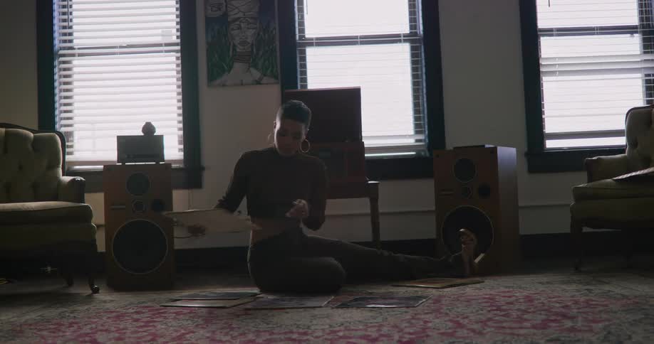 Woman sits on floor near speakers while looking through records