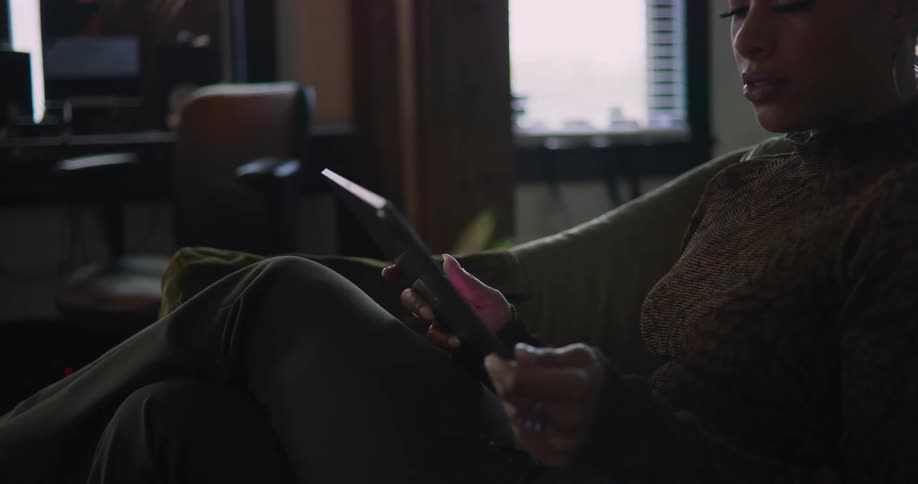 A young woman is sitting on the couch and is using her tablet