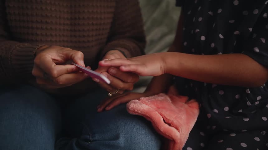 Mother files daughters nails as she gives her a manicure while they sit