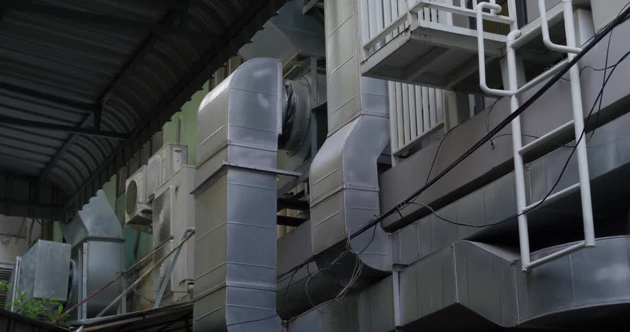 Ladder leads to small platform on building with commercial ducts across from covered area