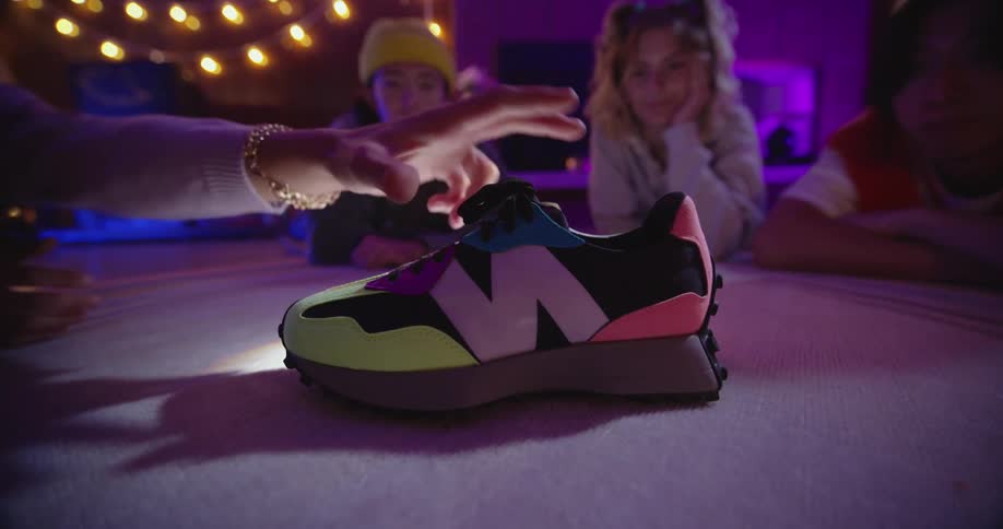 A group of teenagers is sitting at a table inside when one grabs the pair of shoes that is on the table
